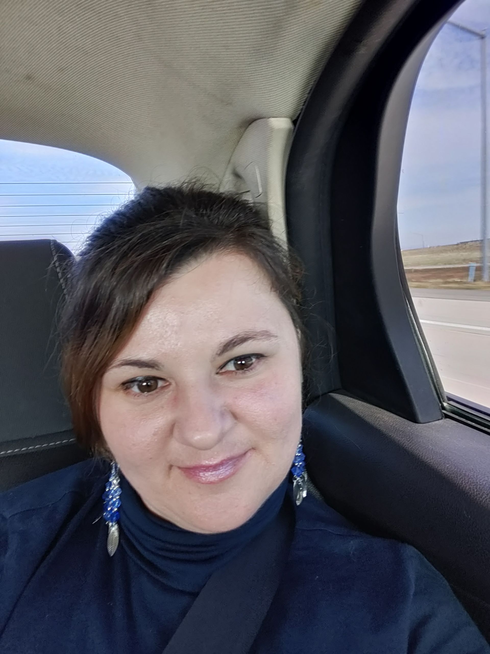 Woman with dark hair and blue earrings smiling in car interior