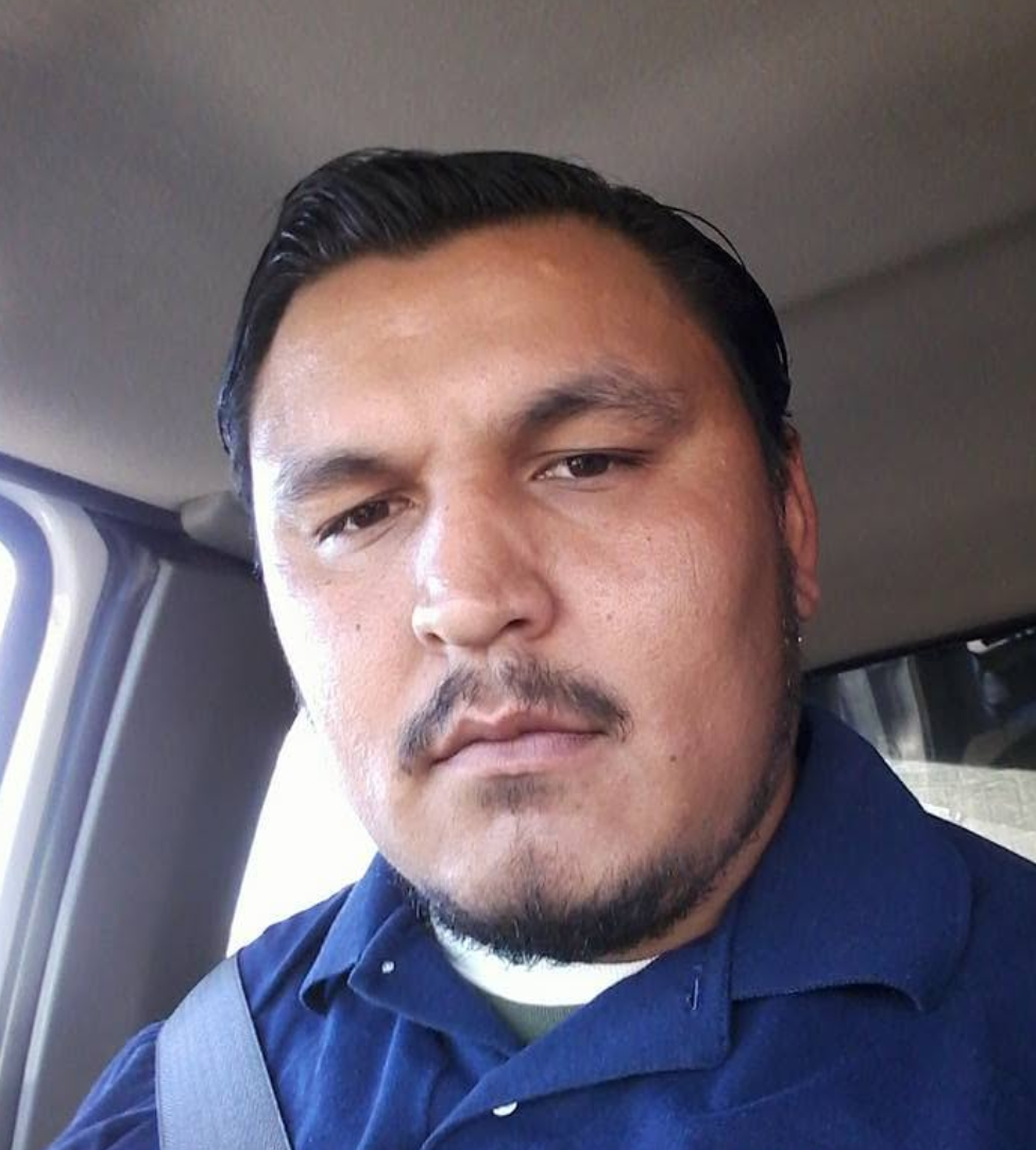 Man with dark hair and goatee wearing blue shirt in vehicle